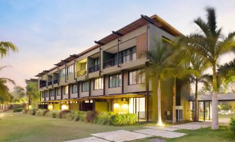 a large building with a long row of windows and balconies is surrounded by palm trees at Mida Resort Kanchanaburi