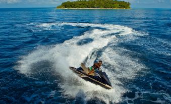 a man is riding a jet ski in the ocean , creating a splash as he goes at Kurumba Maldives