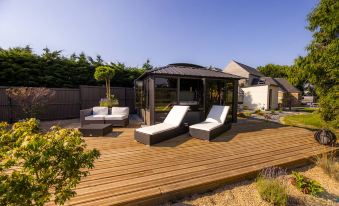 a wooden deck with a gazebo , lounge chairs , and umbrellas , surrounded by a garden and trees at Hôtel la Ramade