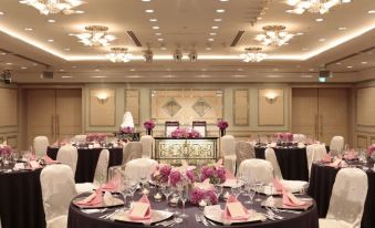 a well - decorated banquet hall with multiple round tables set for a formal event , featuring white chairs and pink flowers at Keio Plaza Hotel Hachioji