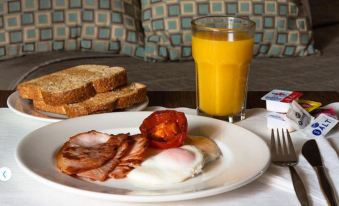 a plate of food with bacon , eggs , and a slice of tomato is next to a glass of orange juice at Bankstown Motel 10