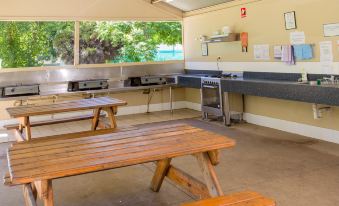 an outdoor kitchen area with wooden tables and benches , as well as a sink and a stove at Shepparton Holiday Park and Village