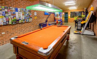 a pool table with a green light fixture above it in an indoor area with brick walls and a wall - mounted light at BIG4 Happy Hallidays