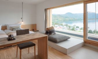 a modern bedroom with a large window overlooking a beautiful view of the ocean , and a wooden desk with a laptop on it at WE Hotel Toya