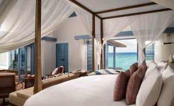 a bedroom with a large bed and canopy , overlooking the ocean through three windows on either side at Raffles Maldives Meradhoo Resort