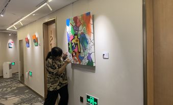 A long hallway adorned with paintings and a hanging art piece spans from one side to the other, creating a visually appealing and artistic atmosphere at Yuzhan No.8 Art Hotel (Shanghai Beach Branch)