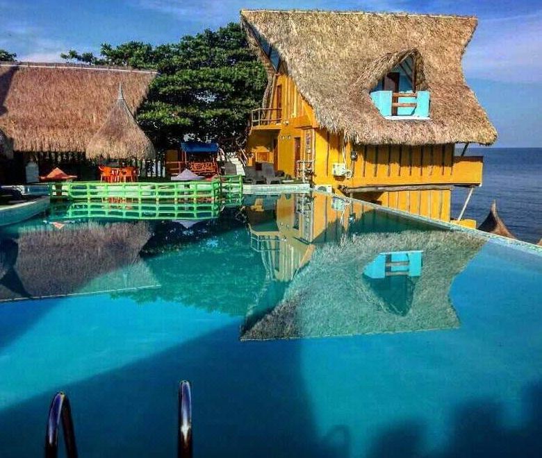 a large pool surrounded by a wooden house , with palm trees in the background and a blue sky above at Riviera Del Sol Hotel Spa