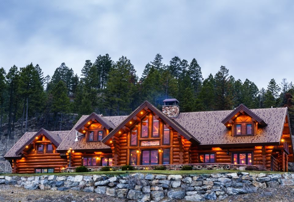 a large log cabin surrounded by trees , with multiple cars parked in front of it at Coyote Bluff Estate