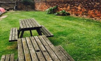 a wooden picnic table and bench set in a grassy area near a brick wall at The Dog Inn