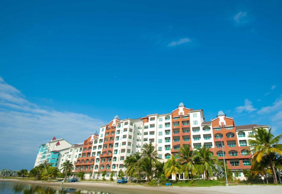 a large white and red apartment building surrounded by palm trees , with a blue sky in the background at Marina Island Pangkor Resort & Hotel