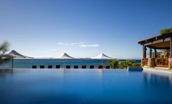 a large , empty swimming pool surrounded by a patio area with chairs and umbrellas , overlooking the ocean at Matamanoa Island Resort