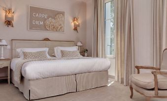 a large bed with white linens and a wooden headboard is in a room with a chair , curtains , and a framed picture on the at Hôtel la Ramade
