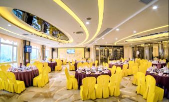 a large dining room with multiple tables covered in yellow tablecloths , and a television mounted on the wall at Royal Hotel