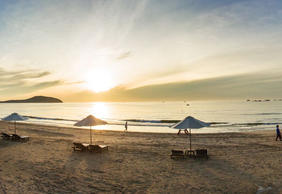 a beach scene with several people enjoying the sun and sand , as the sun sets over the ocean at Pandanus Resort