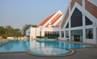 a large swimming pool is surrounded by a building with a red roof and trees in the background at Rimpao Hotel