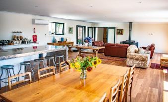 a large , open living space with a wooden dining table , chairs , and couches , surrounded by kitchen appliances and other furniture at Tamar House