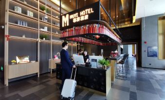 A woman stands in front of the counter at an Asian restaurant with her luggage and other belongings at MUYI Hotel Hongqiao Hub Shanghai
