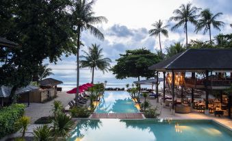 a resort with a large pool surrounded by palm trees and lounge chairs , overlooking the ocean at Anantara Rasananda Koh Phangan Villas
