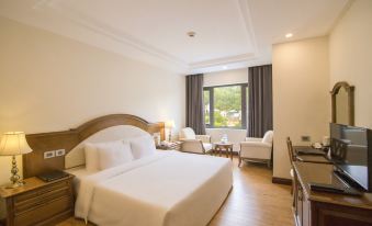 a well - lit hotel room with a white bed , wooden headboard , and couch , along with a window with curtains at Sai Gon Ha Long Hotel