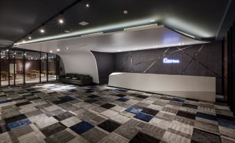 a modern lobby with a gray and white checkered floor , a curved reception desk , and a large sign above the door at Green Hotel