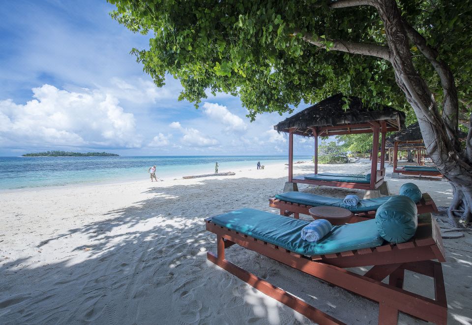 a tropical beach scene with several lounge chairs and umbrellas , providing a relaxing atmosphere for beachgoers at Gangga Island Resort & Spa