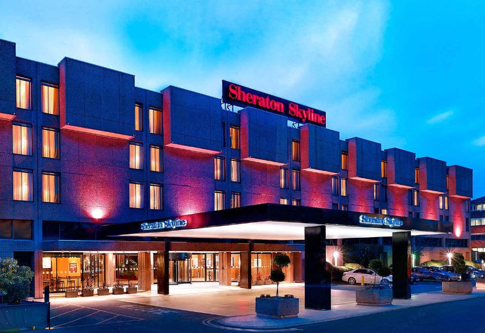 the exterior of a sheraton hotel at night , with the hotel 's name prominently displayed on the building at Sheraton Skyline Hotel London Heathrow