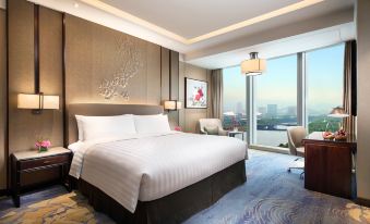 The bedroom features large windows and a balcony that overlook the city, with an elegant bed positioned in front at Shangri-La Yiwu