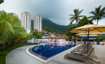 a large outdoor pool surrounded by lounge chairs and umbrellas , with tall buildings in the background at DoubleTree Resort by Hilton Hotel Penang