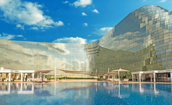 a large swimming pool with a waterfall and lounge chairs in front of a modern building at Okada Manila