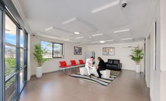 a modern waiting room with two people sitting and standing , surrounded by comfortable seating and plants at ValueSuites Penrith