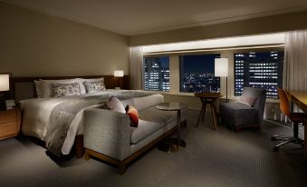 The room has large windows, a bed, and a desk, with an attached sitting area next to it at Keio Plaza Hotel Tokyo