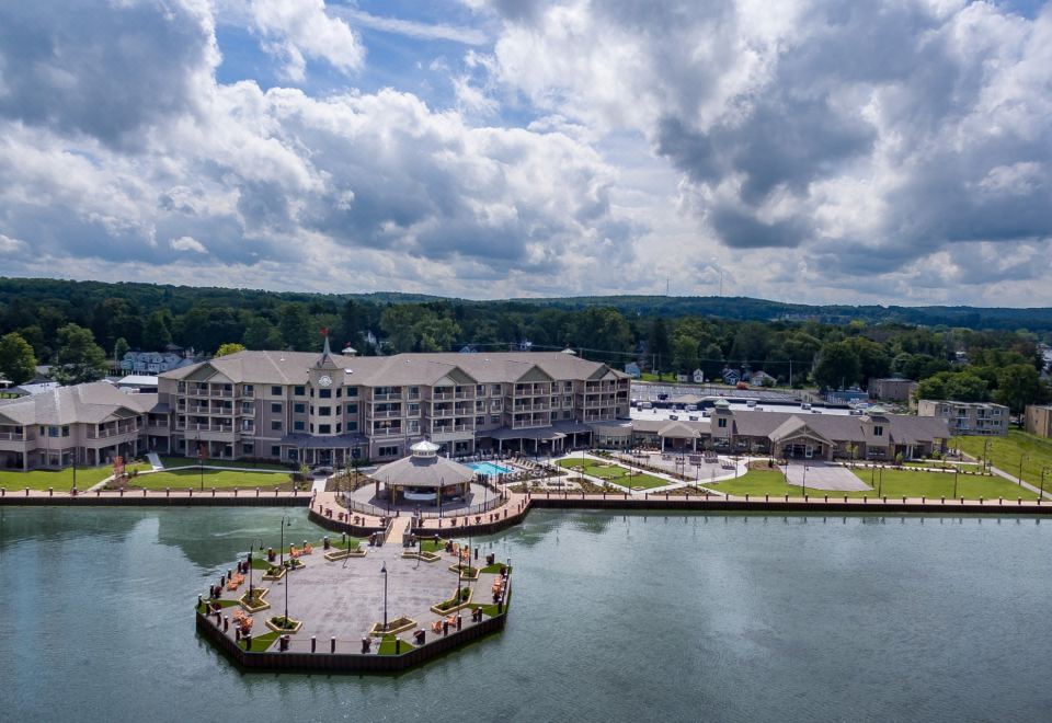 a large , multi - story building with a circular walkway leading to it is situated near a river at Chautauqua Harbor Hotel - Jamestown