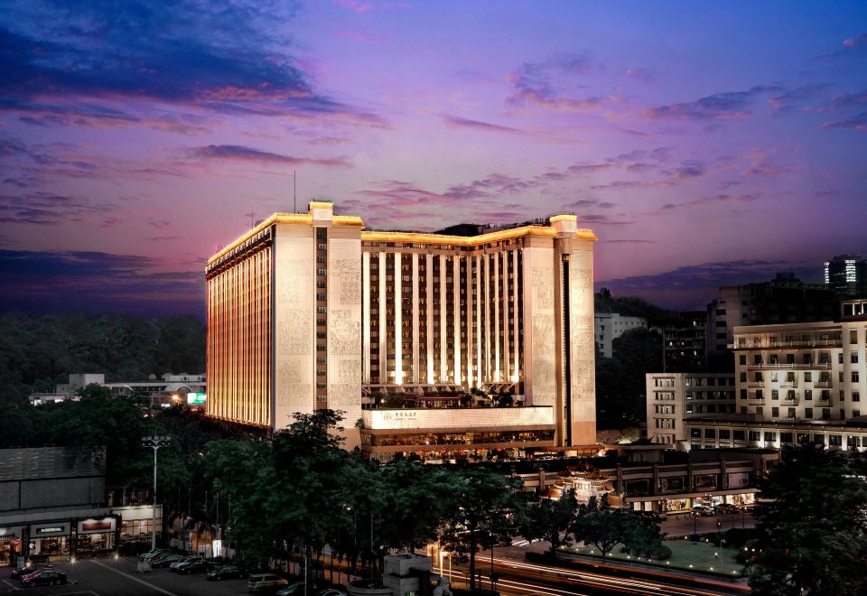 At dusk, a well-lit large building stands in the center, surrounded by other buildings at China Hotel