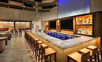 a long bar with wooden stools and a large tv screen in the background , creating a cozy atmosphere at Embassy Suites by Hilton Plainfield Indianapolis Airport