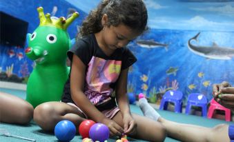 a young girl is playing with colorful balls in a room , surrounded by other children and adults at Holiday Resort Lombok