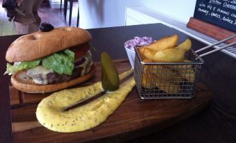 a wooden dining table with a plate of food , including a cheeseburger , fries , and pickles at The Selsey Arms