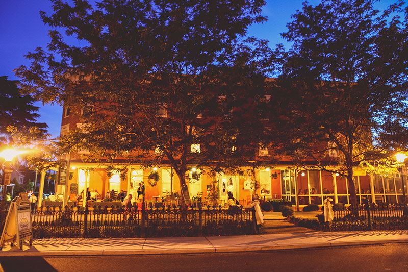 a nighttime scene of a city street with a restaurant on the corner , surrounded by trees and people at Atlantic Hotel