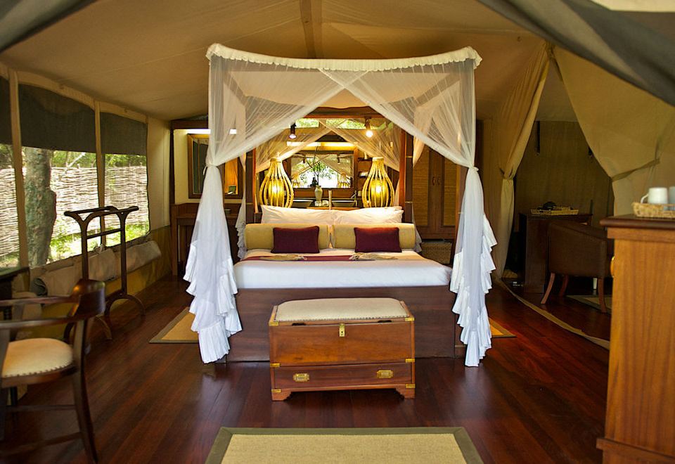 a luxurious bedroom with a canopy bed , wooden floors , and large windows , bathed in natural light at Mara Intrepids Tented Camp