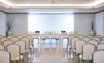 a large , empty conference room with rows of white chairs arranged in a semicircle around a long table at Mitsis Selection Laguna