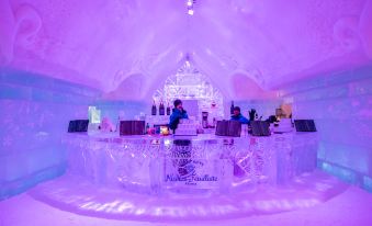 a bartender is behind a bar in an ice bar , surrounded by various bottles and glasses at Hotel de Glace (Ice Hotel)