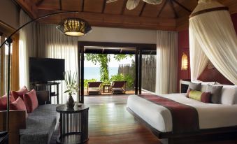 a spacious bedroom with a large bed , a television , and a door leading to a patio overlooking the ocean at Anantara Rasananda Koh Phangan Villas