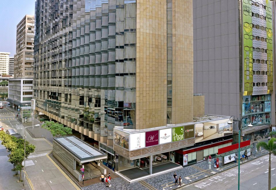 A large building stands on a street with people in front and other buildings behind it at The Kowloon Hotel