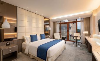 a large bed with white and blue linens is in a room with a desk , chair , and sliding glass door at Grand Palace Hotel