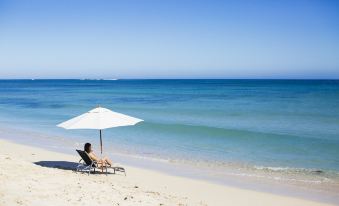 a woman is sitting on a beach chair under an umbrella , enjoying the view of the ocean at Exmouth Escape Resort