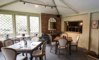 a room with wooden tables and chairs , a brick wall , and large windows overlooking the outdoors at The White Hart