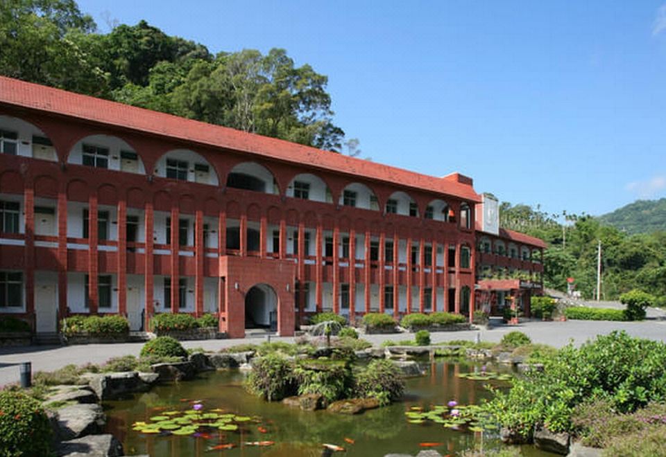 a large red building surrounded by a pond with lily pads , creating a serene and picturesque scene at Rainbow Hotel