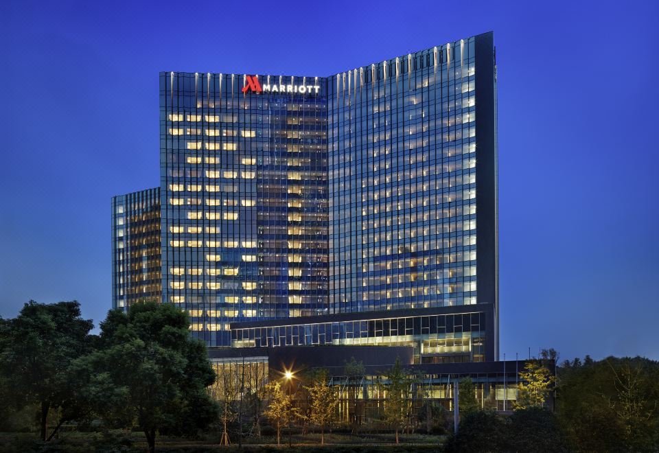"At night, a large illuminated building with the word ""hotel"" on its front stands prominently" at Hangzhou Marriott Hotel Qianjiang