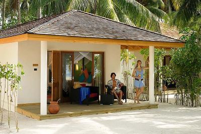 a woman standing in front of a small wooden building , which appears to be a beach house at Vilamendhoo Island Resort & Spa