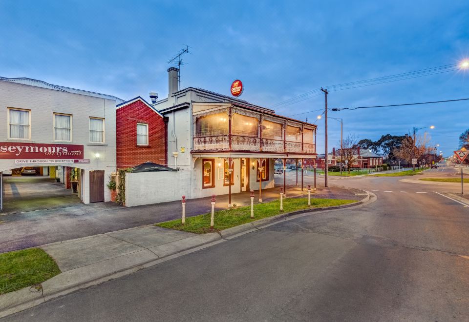 a modern , two - story building with a red roof and white walls , located on a street corner in a residential area at Seymours on Lydiard