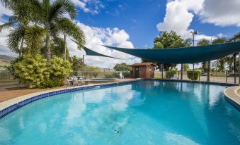 a large swimming pool with a blue tarp covering it , surrounded by palm trees and a clear sky at Big4 Townsville Gateway Holiday Park